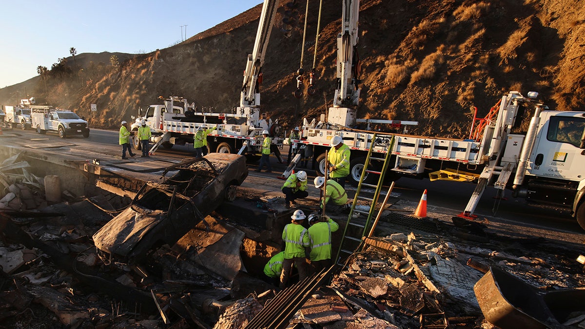 Workers pull a burnt car out of the wreckage of a home destroyed by the Palisades Fire