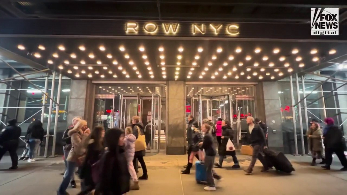 People walk by The Row hotel in Manhttan which has golden lights under the awning