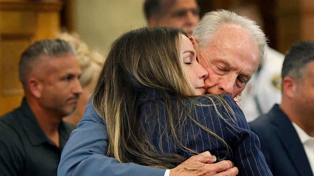 Karen Read hugging her father tenderly in a suit inside a courtroom.