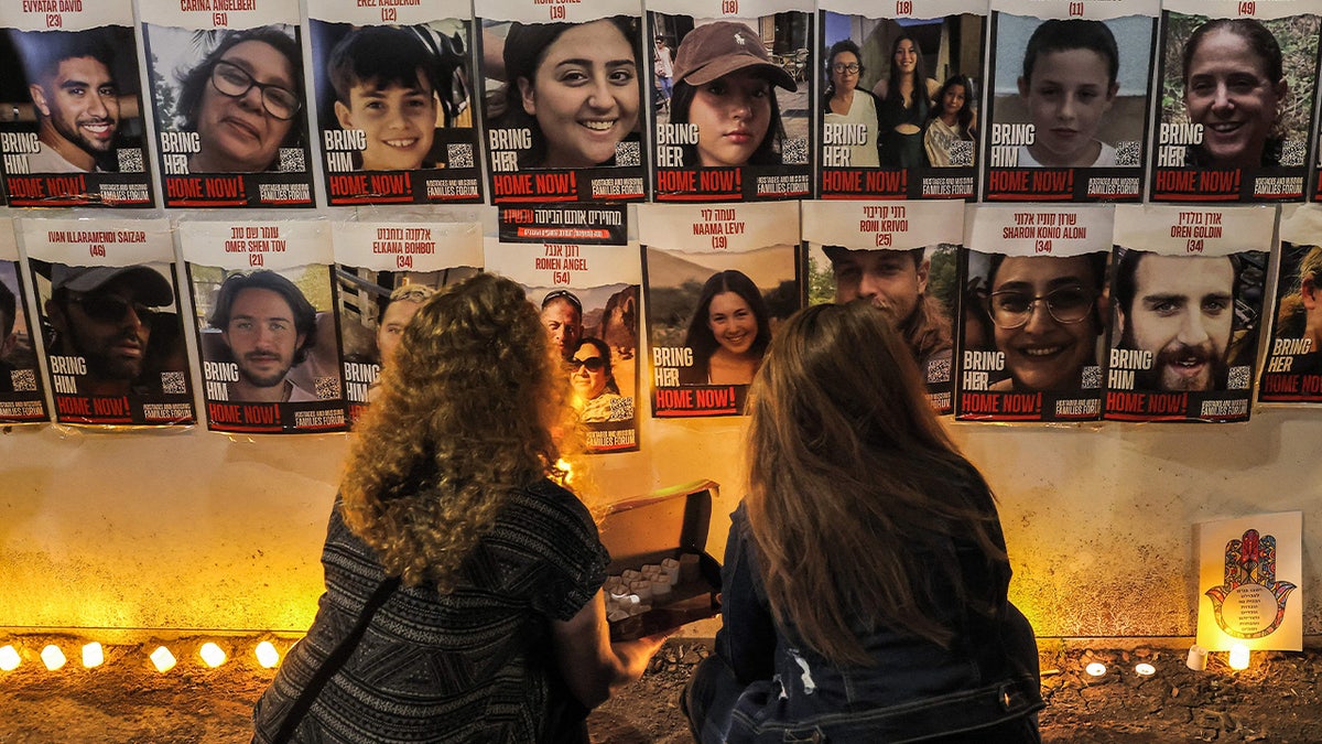 People light candles beneath a wall showing posters identifying hostages abducted by Palestinian militants during the October 7 attack and currently held in the Gaza Strip, at a vigil demanding government action for their return outside the Israeli parliament (Knesset) in Jerualem on November 7, 2023.