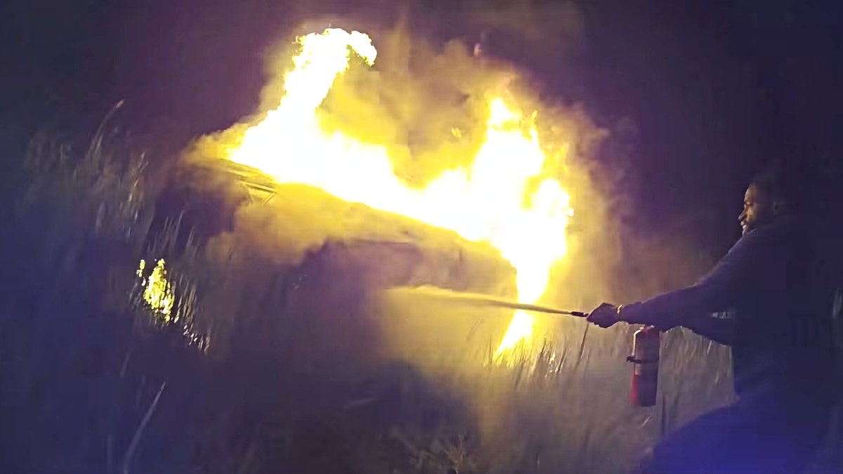 A screenshot of the crash footage showing a Good Samaritan putting out flames with a fire extinguisher