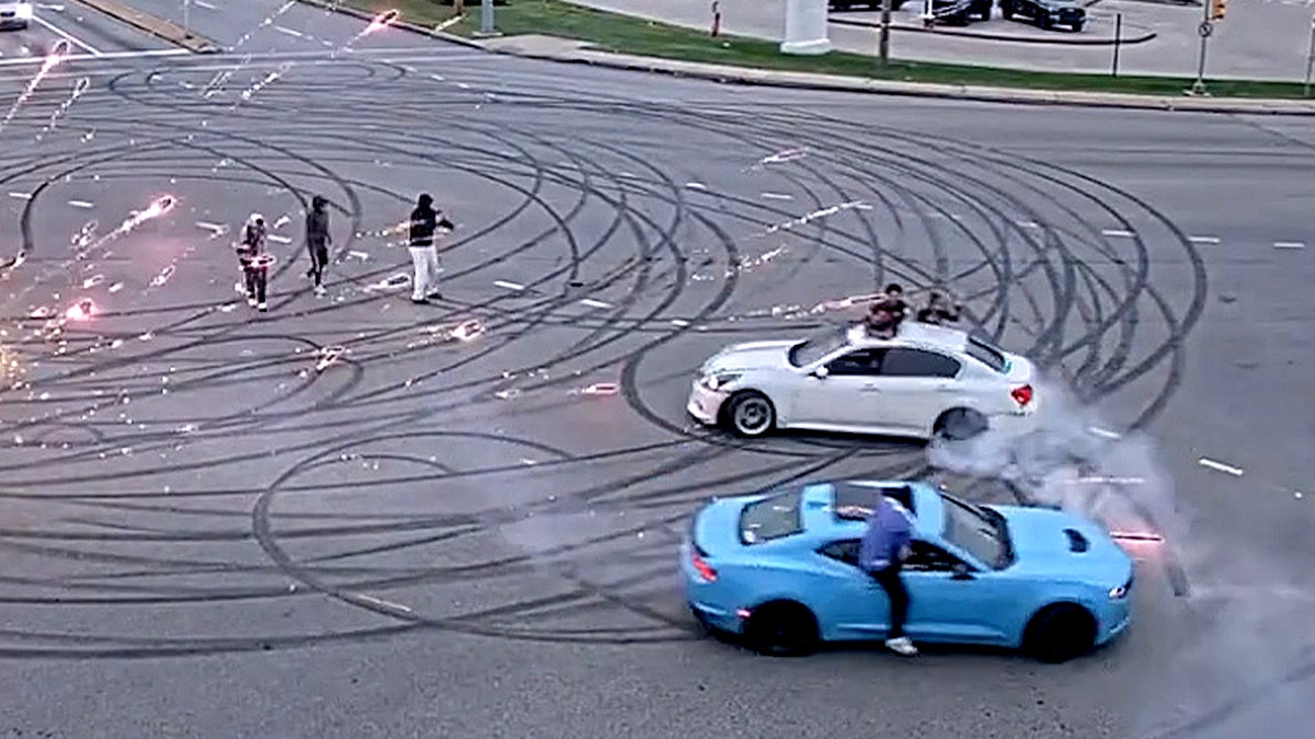 blue and white cars make donuts in large street intersection