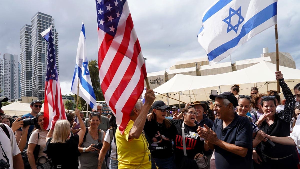 People wave Israeli and American flags while gathering in Hostages Square during a public rally.