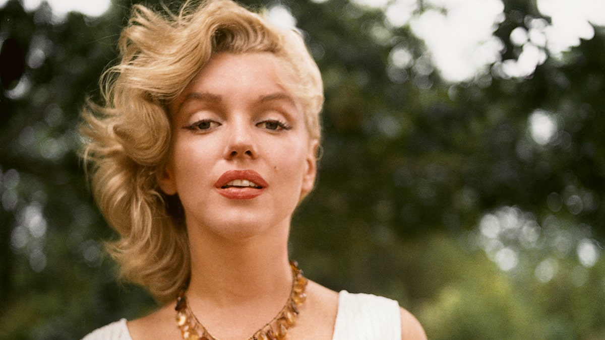 A close-up of Marilyn Monroe outdoors wearing a white dress and a beaded necklace