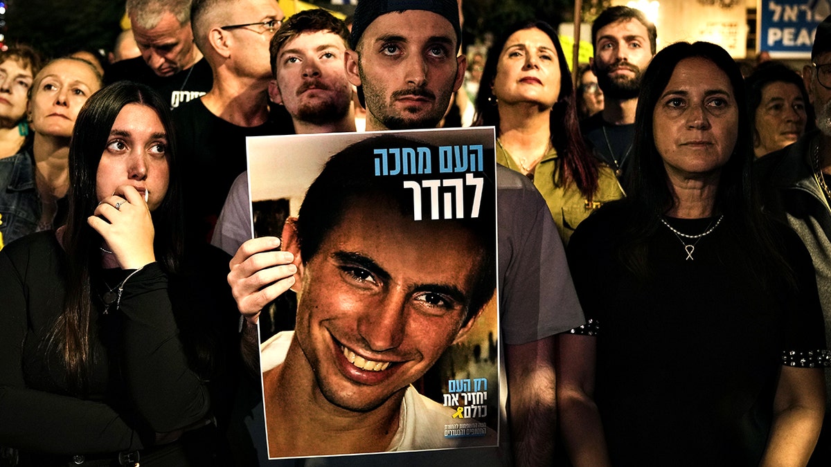 Freed Israeli hostage Matan Angrest holds a photo of Hadar Goldin in crowd of people