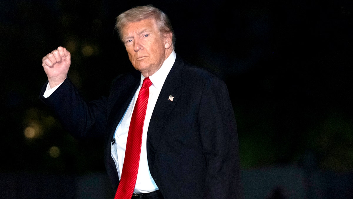 President Donald Trump wearing a dark suit and red tie as he walks with his arm raised in a gesture