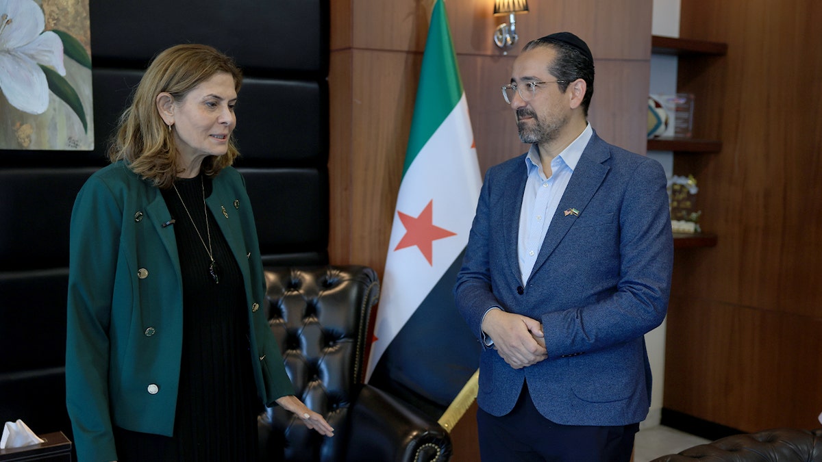 A rabbi and a government minister hold a document together during a ceremony recognizing a new cultural association.