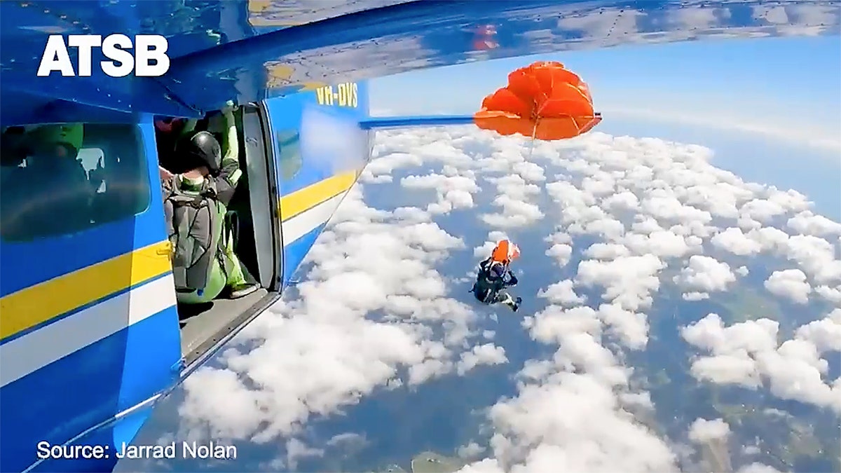 A skydiver drifts beneath a partially opened orange reserve parachute that is caught on the aircraft's wing.