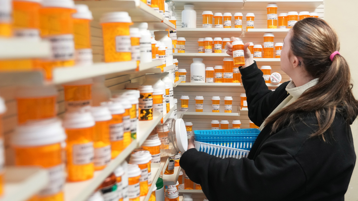 A pharmacy tech pulls medication from a shelf inside a pharmacy
