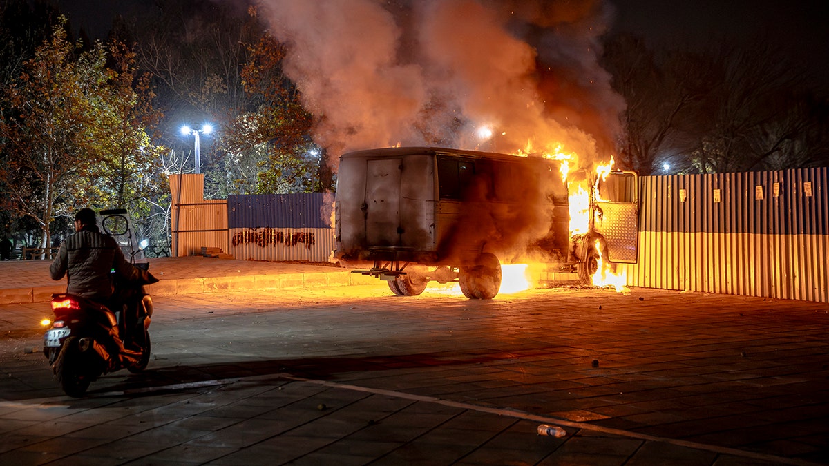 Person on motorcycle near burning vehicle in Tehran, Iran