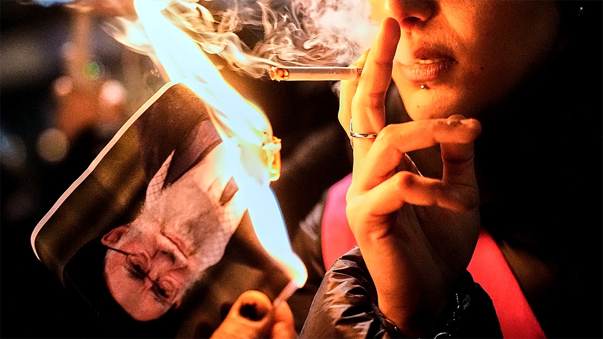 Protesters lighting cigarettes using photo of Ayatollah