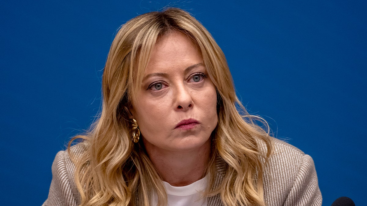 Italy’s prime minister sits at a podium during a formal media briefing.