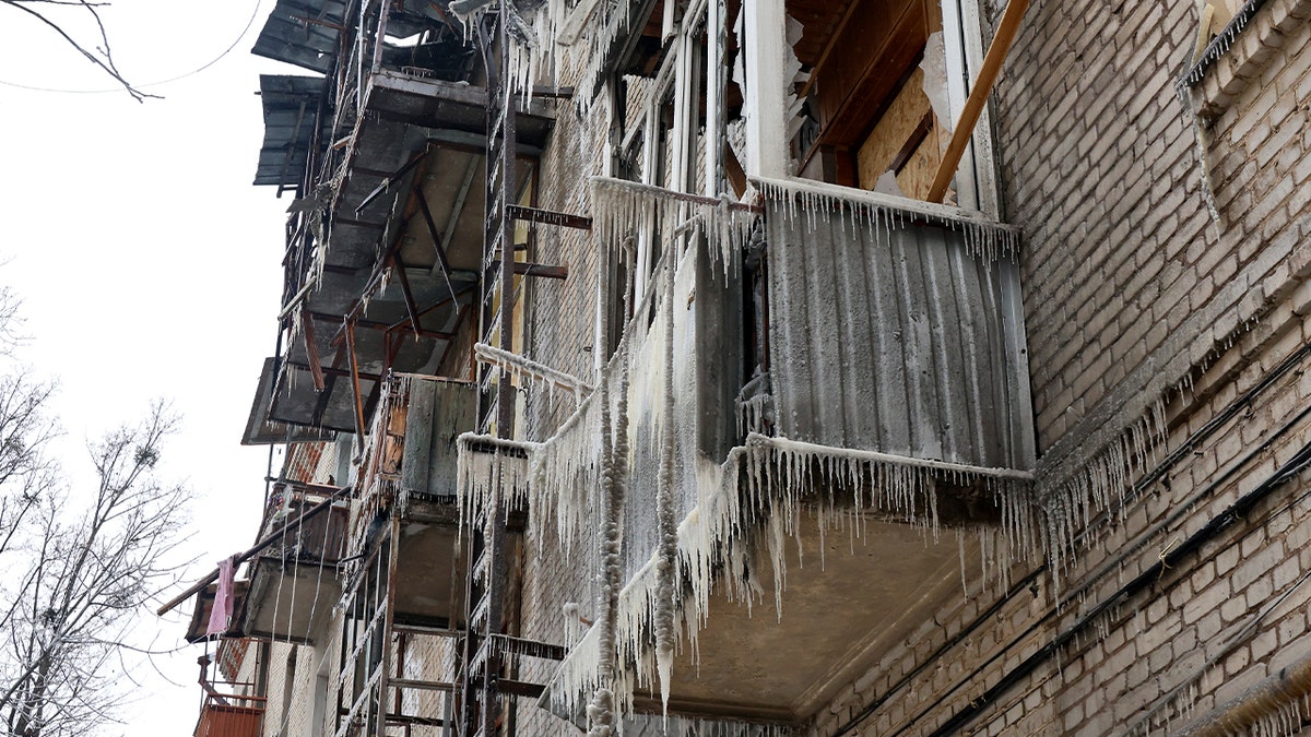 Icicles form along shattered balconies of a damaged apartment building in winter conditions.