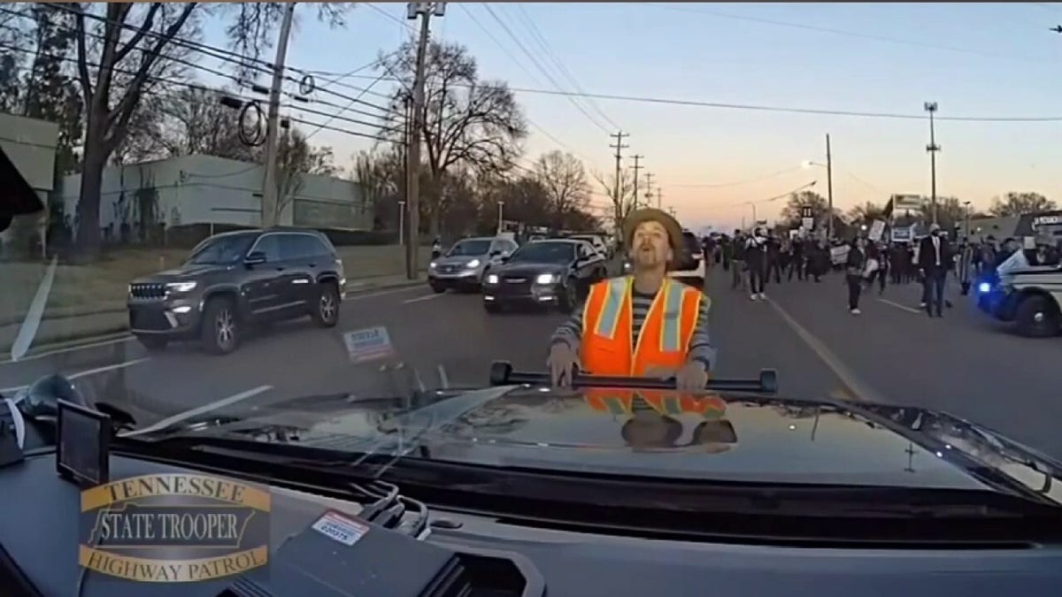 Man falling down while holding onto patrol car.
