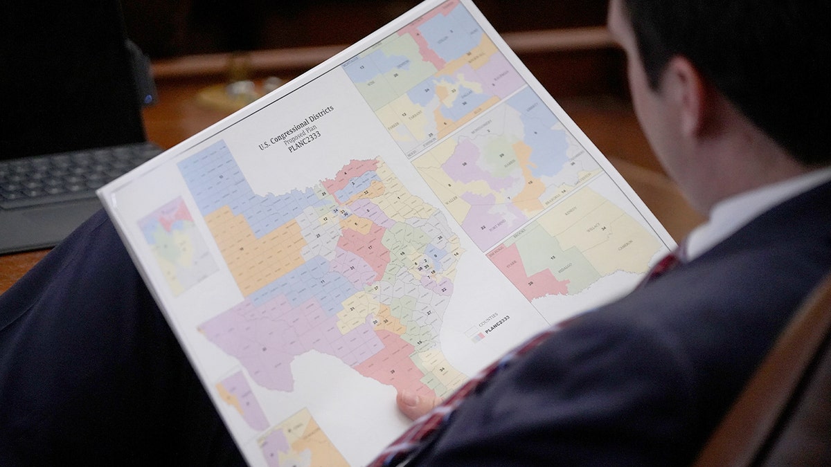 A lawmaker studies a proposed congressional district map while debate unfolds inside the Texas House chamber.