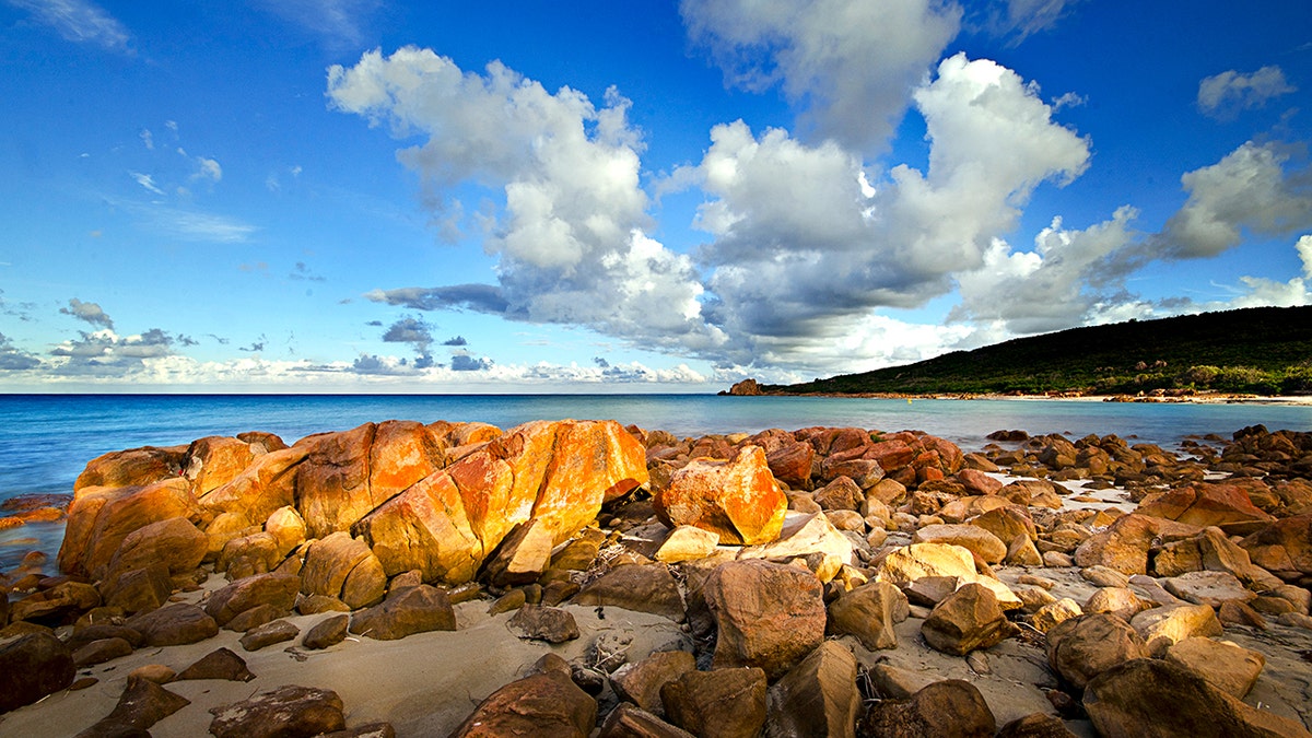 rocks on a shoreline with blue water and skies