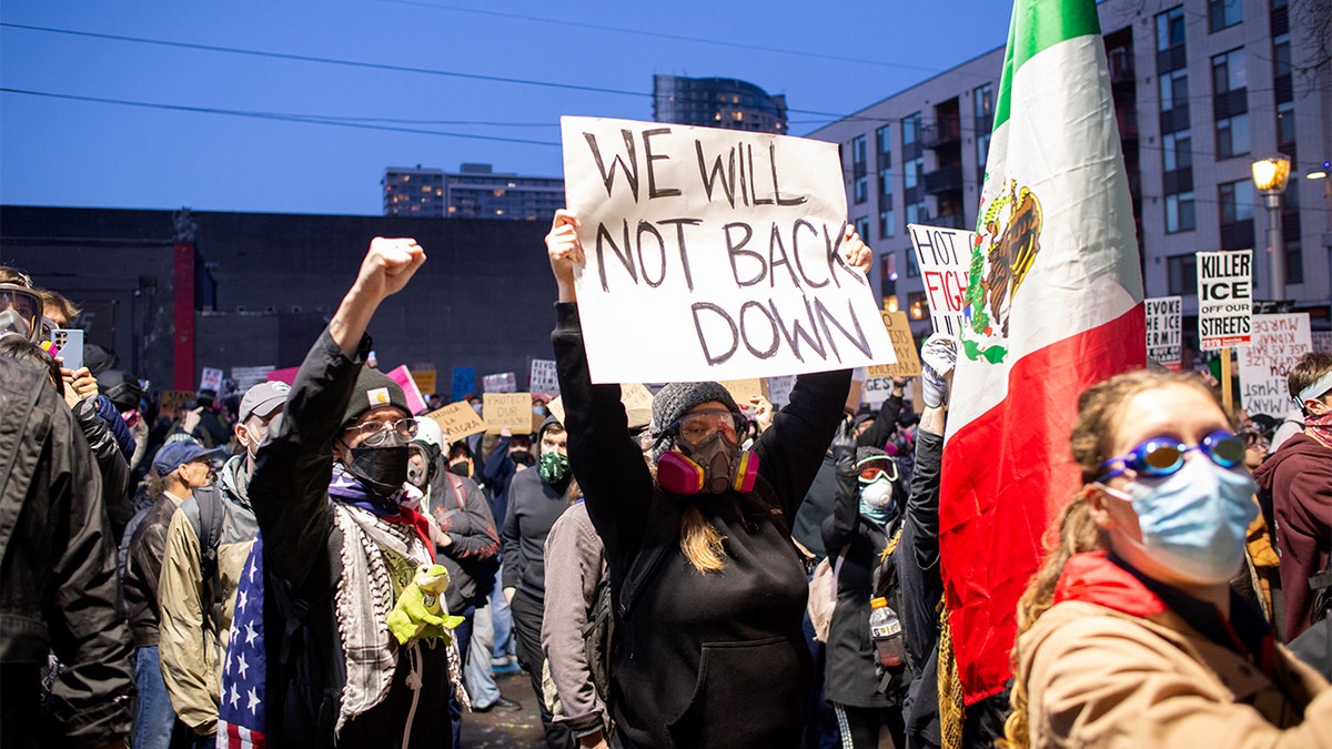 Protesters walk in a large group through downtown streets toward a federal immigration facility.
