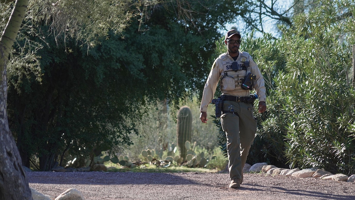 A member of the Pima County Sheriff's office standing on a residential street near Nancy Guthrie's house.