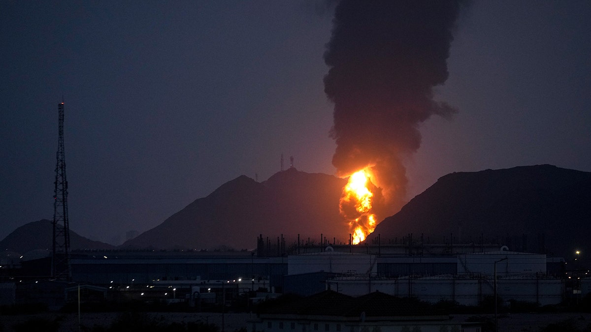 A large fire burning at an industrial facility with a massive plume of dark smoke rising into the sky.