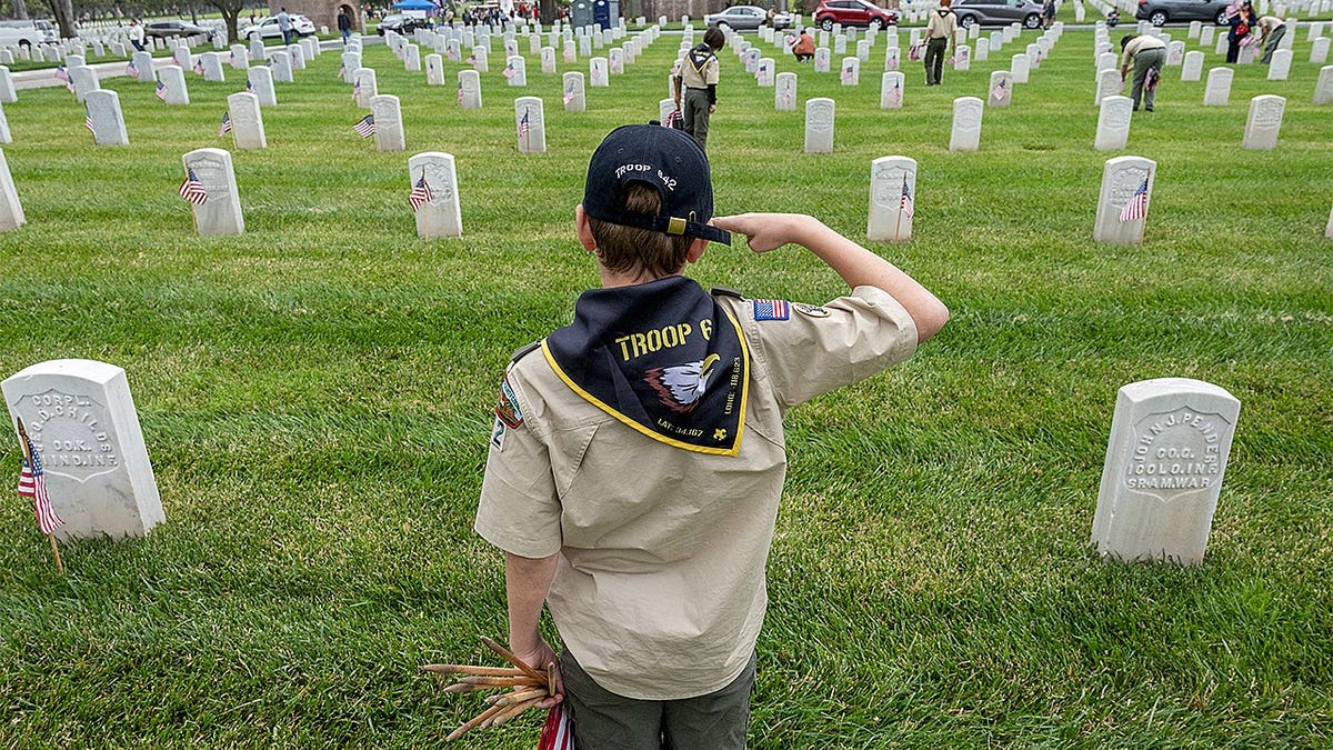 Julian Holkenborg saluting after planting a flag at Los Angeles National Cemetery