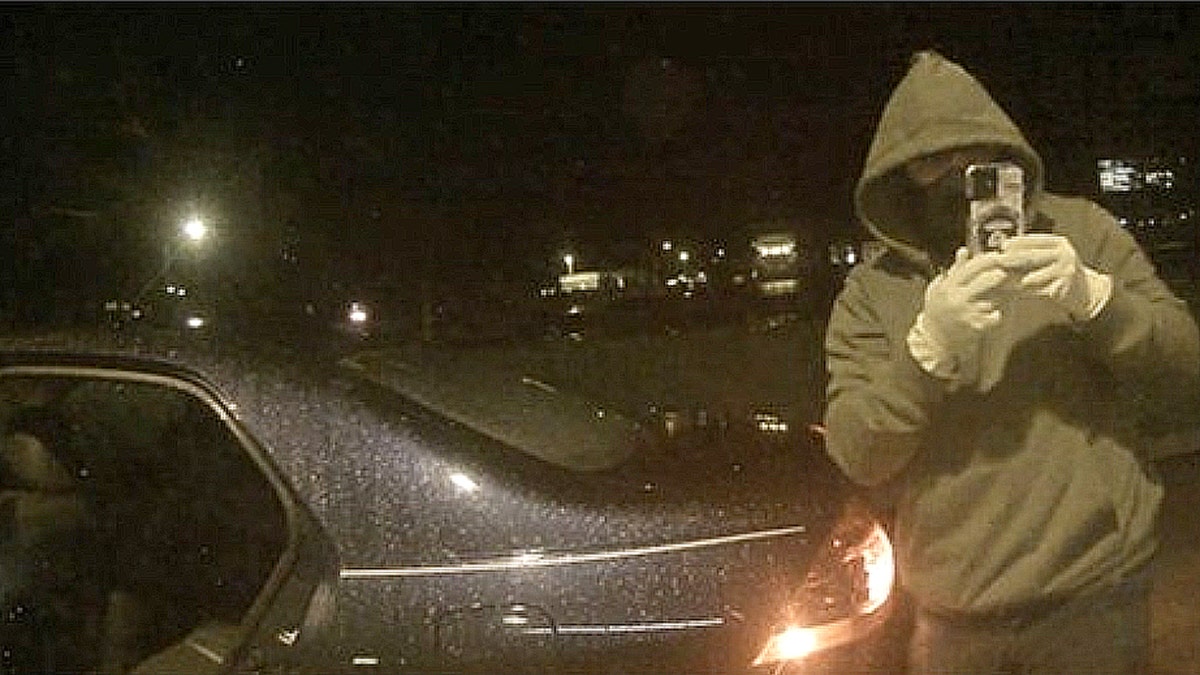 Hooded individual recording ATM during alleged malware jackpotting operation