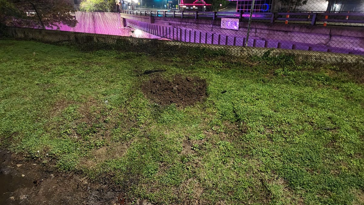 a drainage ditch, grassy area and fence are seen with vehicle marks following the crash