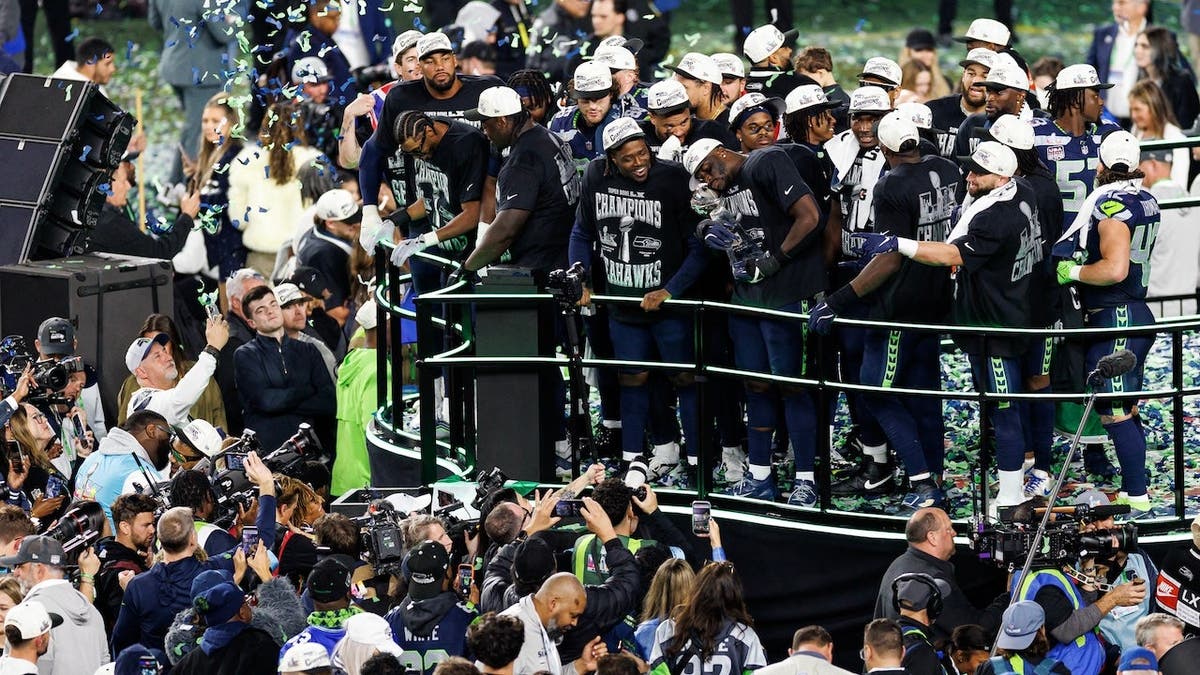 Derick Hall holding the Vince Lombardi trophy on stage with Seattle Seahawks teammates