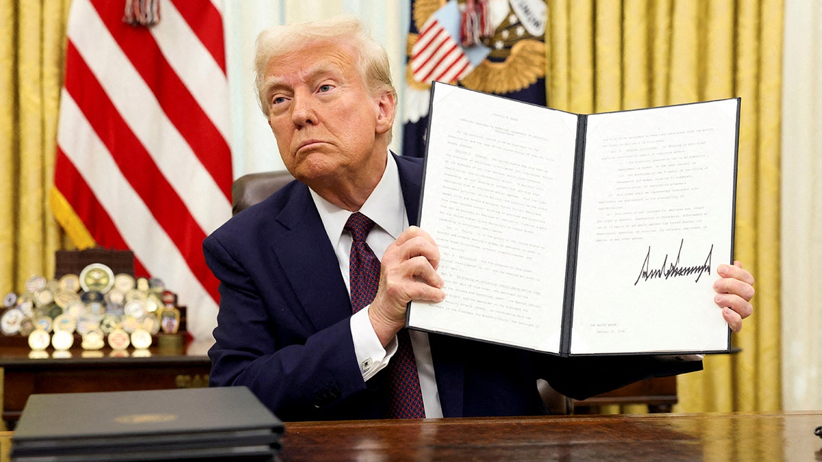 President Donald Trump holding a signed executive order in the Oval Office