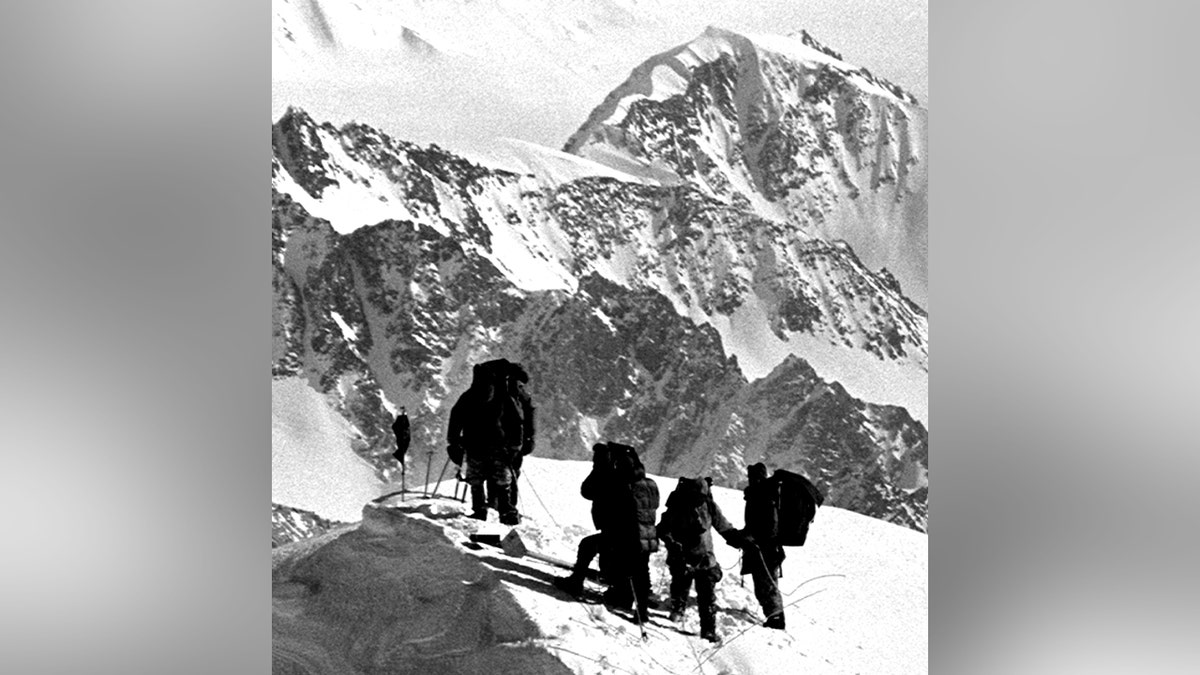 A group of hikers stands atop a snowy mountain.