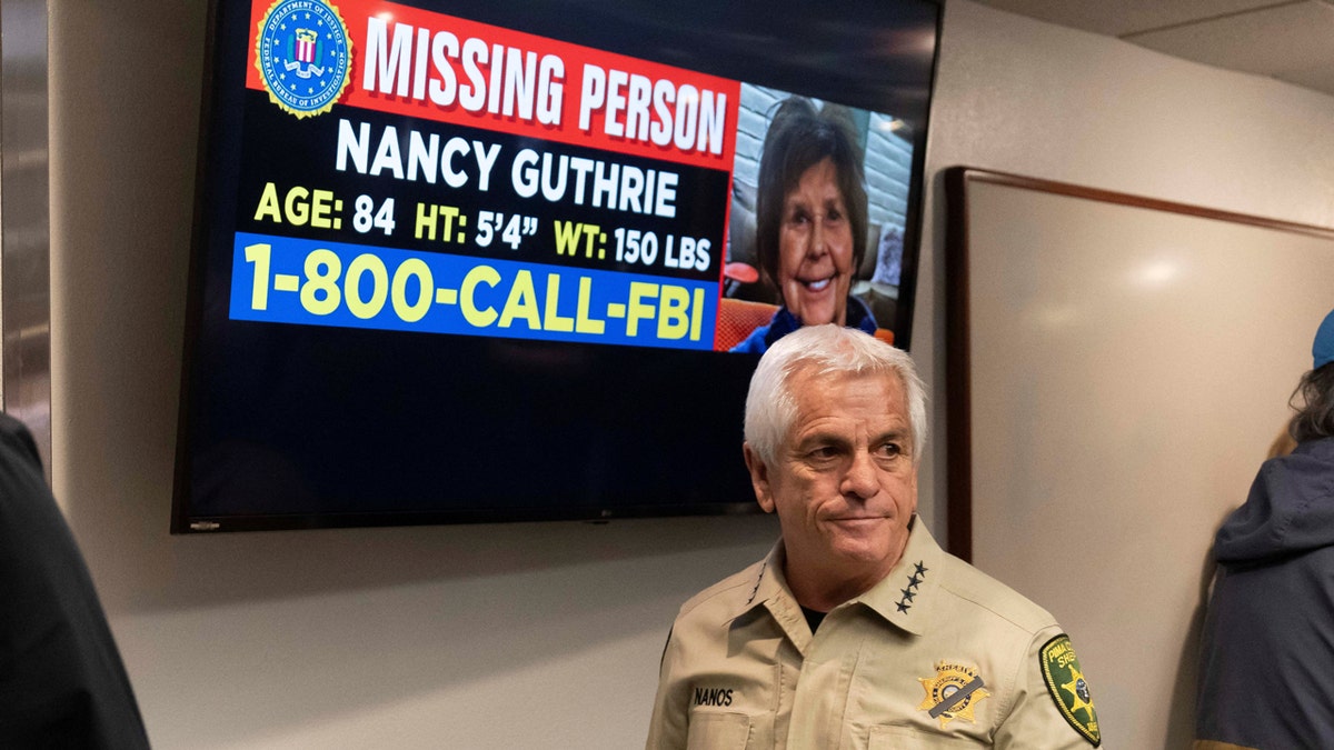 Sheriff Chris Nanos standing in front of a missing persons photo