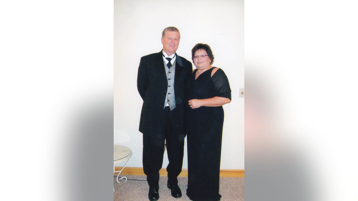 Jeff Walton and Deb Proctor wearing black formal attire against a white wall.