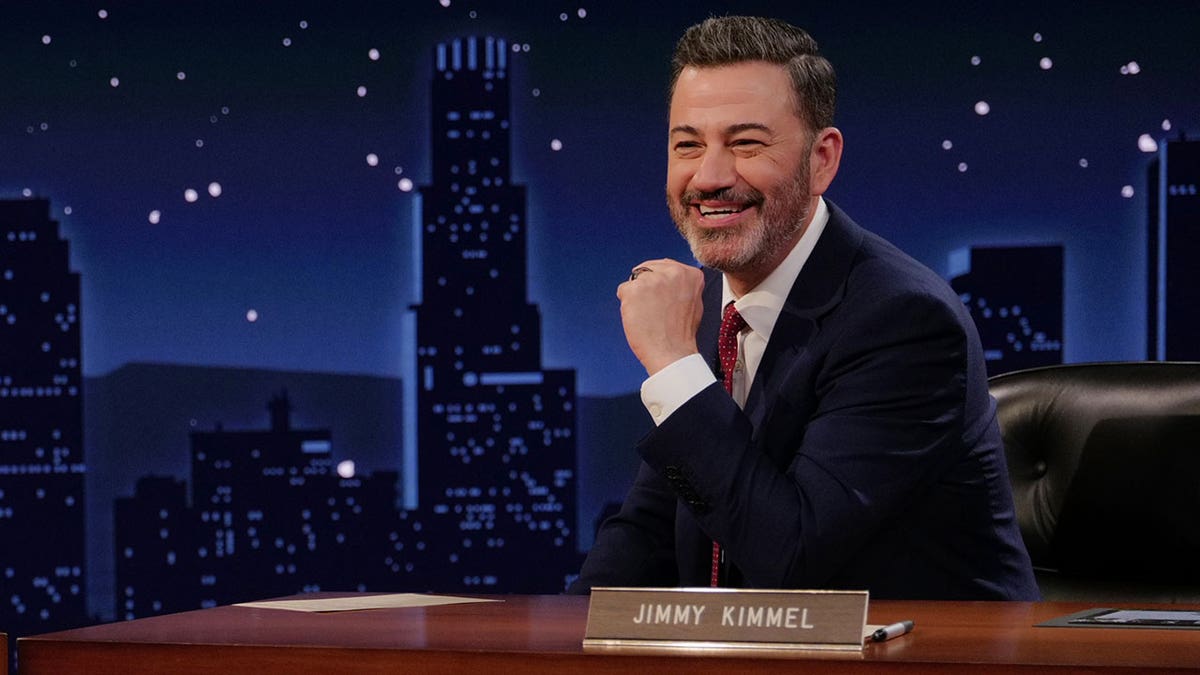 Jimmy Kimmel sitting at a desk on the set of his show