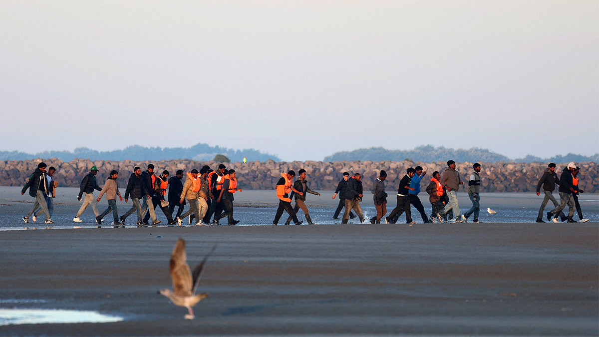 Migrants walking along the beach at Petit-Fort-Philippe near Calais, France
