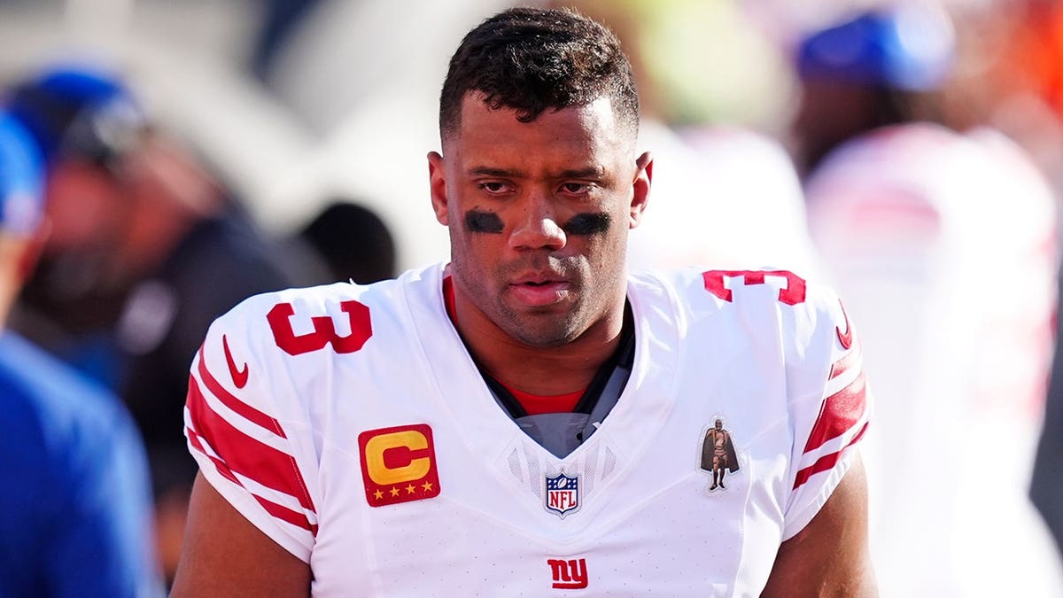 New York Giants quarterback Russell Wilson standing on the sidelines at Empower Field at Mile High