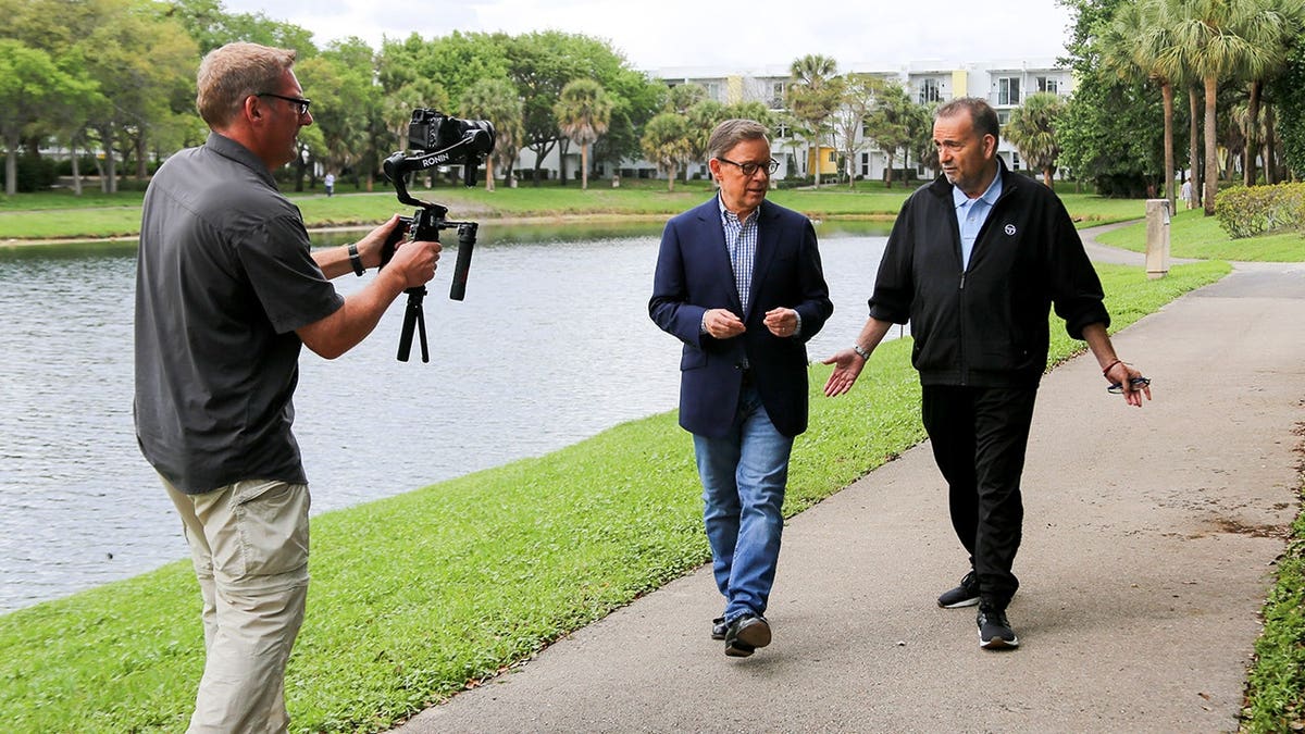 Eric Shawn walks with Lewis Kasman as a cameraman films them.