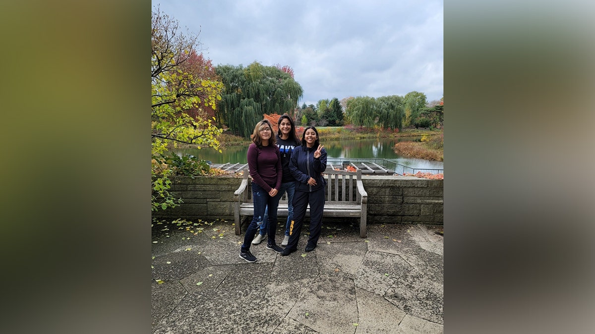 Angelina Resendiz poses with family members in front of a pond surrounded by autumn foliage.