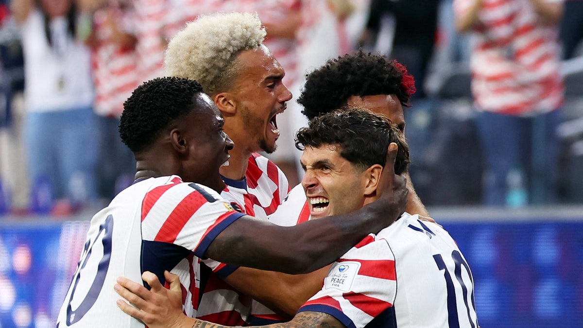 Christian Pulisic celebrating with teammates on the soccer field.