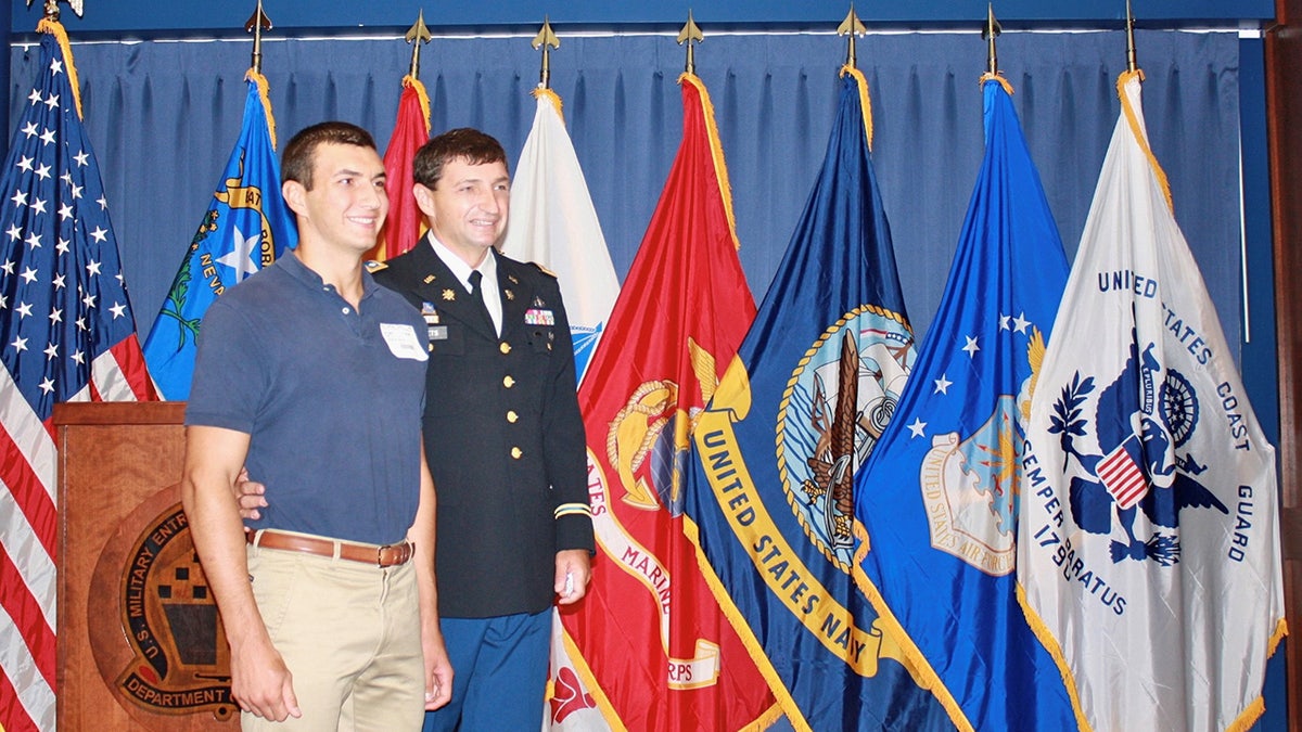 Nicholas Douglas Quets and his father standing in front of flags