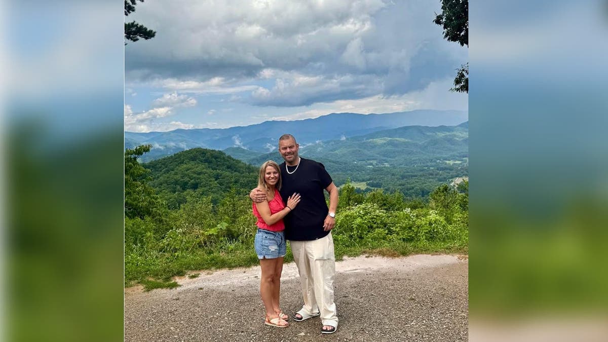 photo shows Hummel and her husband posing with trees and hills in backdrop