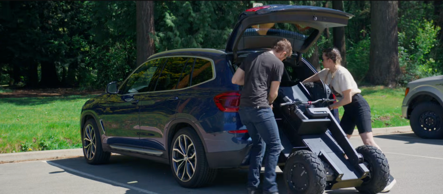 two people loading the folded UPT chassis into a BMW SUV