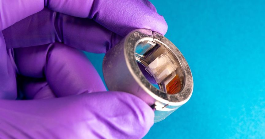 A purple-gloved hand holding a smart ring.