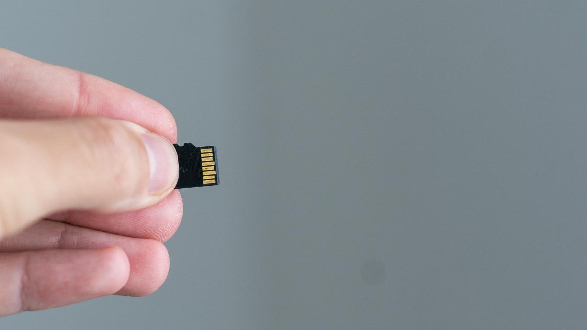 Fingers hold a small microSD card.