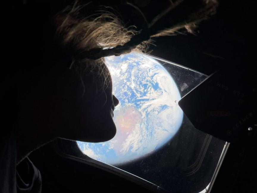 Astronaut’s face in profile against the view of the Earth from the craft’s window. Her dangling braid is also visible.