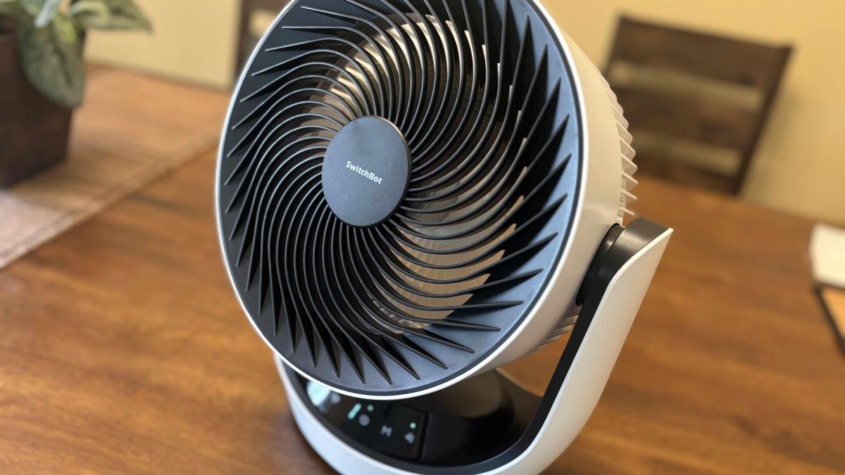 A white SwitchBot fan on a wood table.