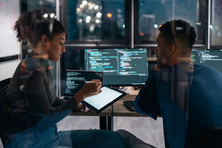 Two Software developers in modern office collaborating analysing the coding on computer screen.