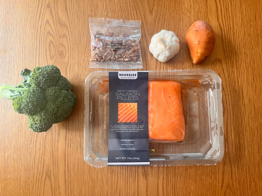salmon, broccoli, a sweet potato, garlic and pecans sitting on a countertop