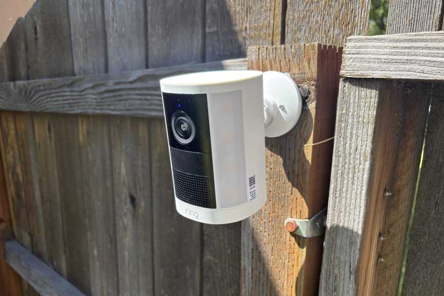 A white Ring Spotlight camera attached to an old wood fence.