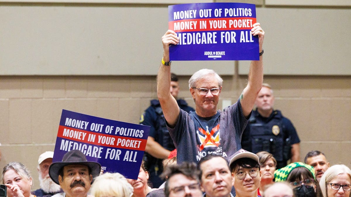 Progressive supporters at a joint rally for U.S. Senate candidate Abdul El-Sayed and U.S. House of Representatives candidate Will Lawrence hold up signs during a rally with U.S. Sen. Bernie Sanders and U.S. Rep. Alexandria Ocasio-Cortez in Lansing, Mich., on July 19, 2026.