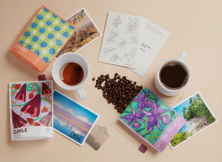 A couple different coffee packets and postcards from Atlas Coffee Club sit next to two cups of coffee.