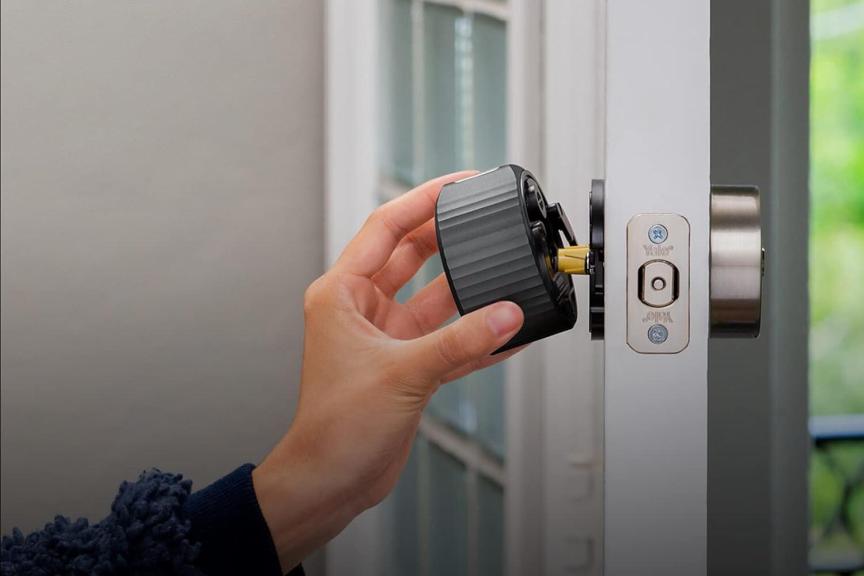 A hand holds the August Home Smart Lock 4 as it's installed on a white door.